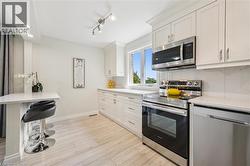 Bright kitchen featuring stainless steel appliances, white cabinetry, a built-in breakfast bar, recessed lighting, and wood-finish flooring - 