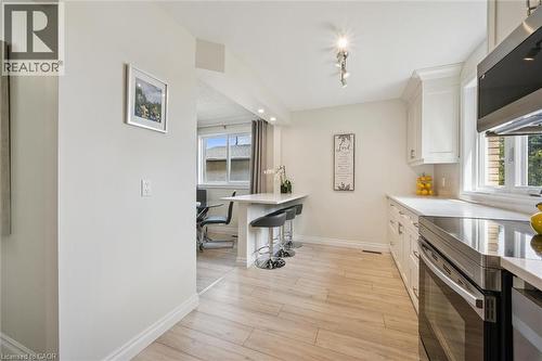 Kitchen featuring wood-finish flooring, white cabinetry, integrated stainless steel appliances, and a breakfast bar with seating - 97 Bechtel Drive, Kitchener, ON - Indoor Photo Showing Kitchen