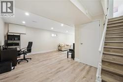 Spacious lower level featuring light wood-finish flooring, recessed lighting, a neutral color palette, a visible window, and a finished staircase with white risers and handrail - 