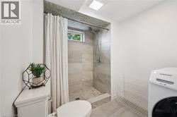 Shower with light grey tile surround, recessed window, and white shower curtain - 