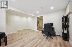 Open concept room featuring wood-finish flooring, recessed lighting, and a white painted staircase with a railing - 
