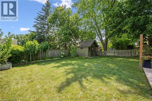 Expansive green lawn featuring a detached shed with a gable roof, mature trees, wood privacy fencing, and a white picket fence - 97 Bechtel Drive, Kitchener, ON - Outdoor With Backyard
