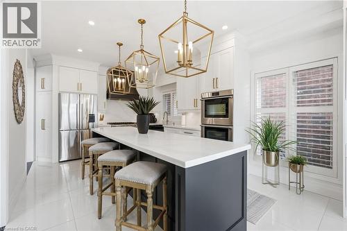 Modern kitchen featuring a large island with white countertop, white cabinetry with gold-tone hardware, stainless steel appliances, and white tile flooring - 47 Winners Way, Binbrook, ON - Indoor Photo Showing Other Room