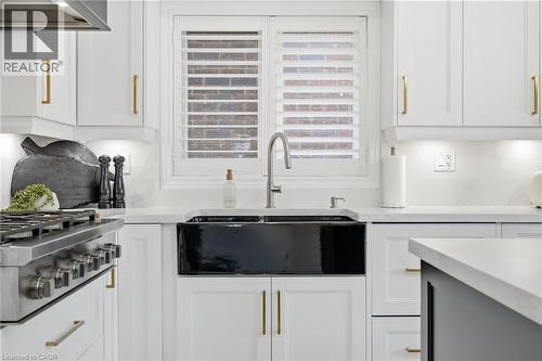 Kitchen featuring a black farmhouse-style sink, stainless steel gooseneck faucet, white shaker cabinetry with gold-toned hardware, white solid surface countertops, and a stainless steel professional-s - 47 Winners Way, Binbrook, ON - Indoor Photo Showing Kitchen