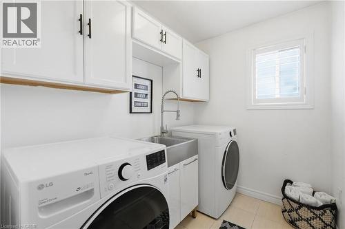 Dedicated laundry area featuring white shaker-style cabinetry with matte black hardware, a stainless steel utility sink with a gooseneck faucet, and a window with white plantation shutters - 47 Winners Way, Binbrook, ON - Indoor Photo Showing Laundry Room