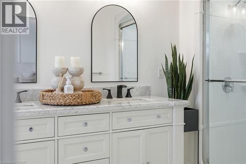 Dual sink vanity with white cabinetry, stone countertop, matte black faucets, and arched mirrors - 47 Winners Way, Binbrook, ON - Indoor Photo Showing Bathroom