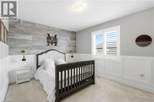 Bedroom featuring a whitewashed wood-finish accent wall, white wainscoting, and a window with plantation shutters - 47 Winners Way, Binbrook, ON - Indoor Photo Showing Bedroom