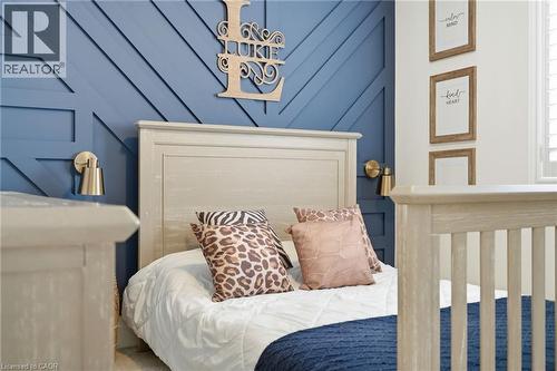 Accent wall with geometric paneling, featuring a light-toned wooden headboard, brushed brass wall sconces, and white window shutters - 47 Winners Way, Binbrook, ON - Indoor Photo Showing Bedroom