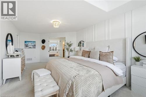 Carpeted bedroom featuring a white upholstered bed frame, a feature wall with vertical paneling, and a chandelier-style ceiling light - 47 Winners Way, Binbrook, ON - Indoor Photo Showing Bedroom