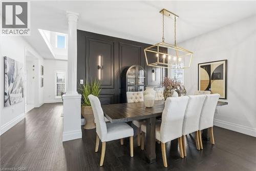 Formal dining area featuring dark wood-finish flooring, a decorative wall panel, and a gold-finish geometric chandelier - 47 Winners Way, Binbrook, ON - Indoor Photo Showing Dining Room