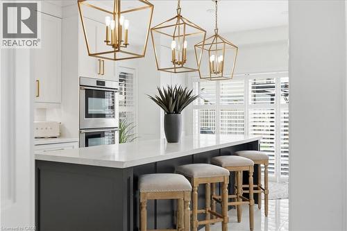 Kitchen featuring a large island with a light-toned countertop, dark base cabinetry, and three brass geometric pendant lights - 47 Winners Way, Binbrook, ON - Indoor