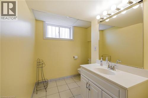 Bathroom featuring a window with security bars, white subway tile flooring, a white vanity with a single sink, a large wall-mounted mirror, and a strip light fixture with multiple bulbs - 217 Lawnhurst Court, Hamilton, ON - Indoor Photo Showing Bathroom