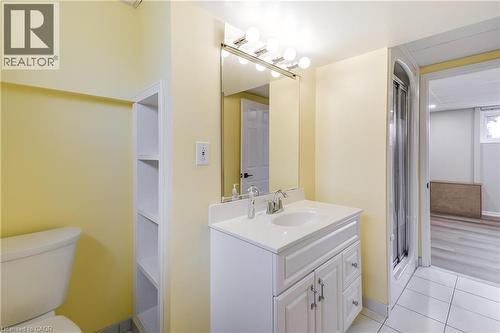 Bathroom with a vanity featuring a white countertop and base cabinet, a wall-mounted mirror with overhead lighting, a built-in shelving unit, and a shower enclosure - 217 Lawnhurst Court, Hamilton, ON - Indoor Photo Showing Bathroom