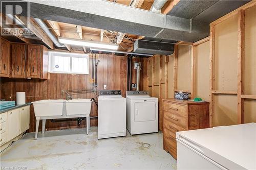 Utility area featuring exposed ceiling joists, wood paneling, a double utility sink, and overhead cabinetry - 217 Lawnhurst Court, Hamilton, ON - Indoor Photo Showing Laundry Room