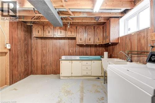 Utility room with wood paneling, exposed ceiling joists, white painted concrete floor, upper cabinetry, and a utility sink - 217 Lawnhurst Court, Hamilton, ON - Indoor