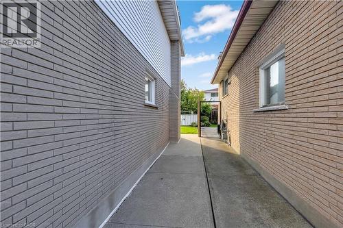 Concrete walkway providing access along the side of the property, featuring two distinct brick-clad exterior walls - 217 Lawnhurst Court, Hamilton, ON - Outdoor With Exterior