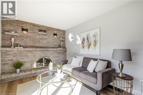 Stone veneer accent wall featuring a brass-trimmed fireplace with an arched opening, wood-finish flooring, and light gray painted walls - 217 Lawnhurst Court, Hamilton, ON - Indoor Photo Showing Living Room With Fireplace