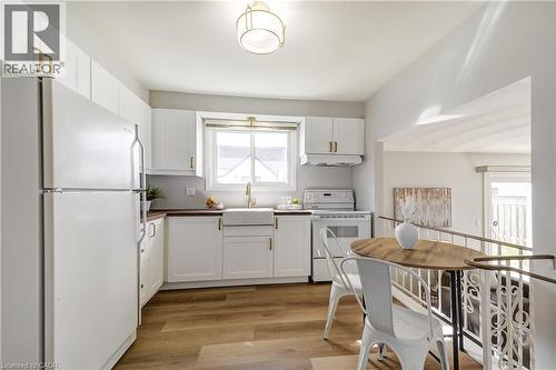 Bright kitchen featuring white cabinetry, wood-finish flooring, a farmhouse-style sink, and a white appliance suite - 217 Lawnhurst Court, Hamilton, ON - Indoor Photo Showing Kitchen
