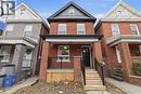 Red brick facade featuring a covered porch with black railings, wood-look steps, and a contrasting black front door - 149 Lottridge Street, Hamilton, ON  - Outdoor With Facade 