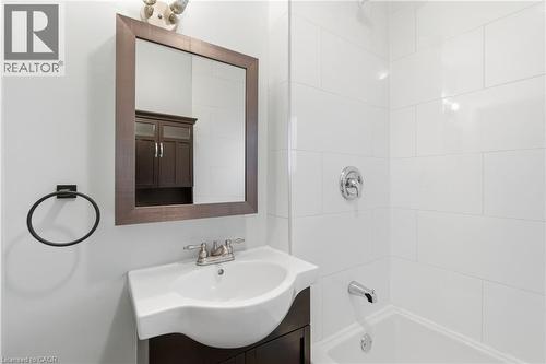 Bathroom featuring a white bathtub and shower with white rectangular wall tiles, a vanity with a white basin sink and dark wood-finish cabinetry, a framed mirror, and a matte black towel ring - 149 Lottridge Street, Hamilton, ON - Indoor Photo Showing Bathroom
