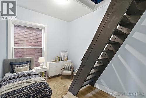 Interior room featuring light blue walls, wood-finish flooring, a single window, and an exposed dark wood staircase - 149 Lottridge Street, Hamilton, ON - Indoor Photo Showing Bedroom