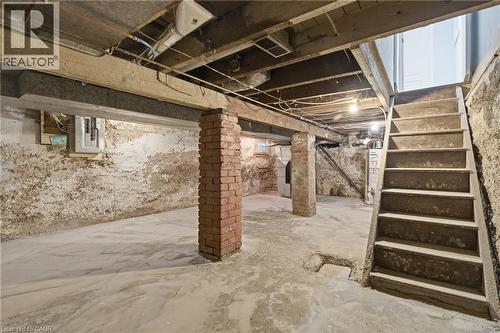 Concrete flooring in an unfinished basement featuring exposed ceiling joists, brick support pillars, a concrete staircase, and a visible electrical panel - 149 Lottridge Street, Hamilton, ON - Indoor