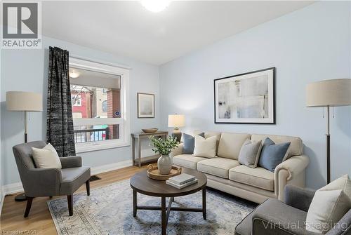 Living area featuring wood-finish flooring, light blue wall paint, a large window with white trim, a ceiling-mounted light fixture, and a decorative area rug - 149 Lottridge Street, Hamilton, ON - Indoor Photo Showing Living Room
