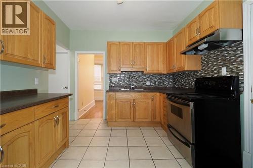 Kitchen featuring light wood cabinetry, a mosaic tile backsplash, stainless steel appliances, dark countertops, and tile flooring - 205 Duke Street E, Kitchener, ON - Indoor Photo Showing Kitchen