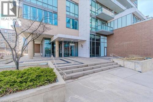 Modern building entrance featuring a prominent address number, glass doors, and a combination of brick and glass exterior - 85 Duke Street W Unit# 507, Kitchener, ON - Outdoor With Balcony
