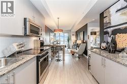 Modern kitchen featuring light gray cabinetry, stainless steel appliances, speckled stone countertops, and a subway tile backsplash - 