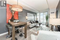 Open-concept living space featuring wood-finish flooring, a contemporary ceiling light fixture, floor-to-ceiling windows, and a glass-paneled balcony - 