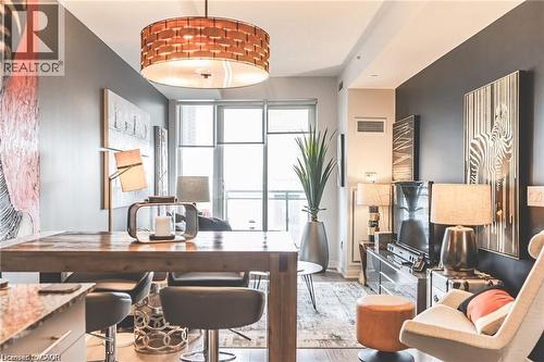 Open-concept living space featuring a wood-finish dining table, dark accent wall, and a large drum pendant light fixture - 85 Duke Street W Unit# 507, Kitchener, ON - Indoor Photo Showing Dining Room