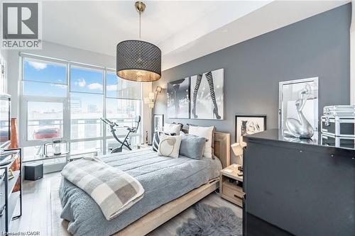 Floor-to-ceiling windows with roller shades, wood-finish flooring, a contemporary drum pendant light, and a neutral color palette - 85 Duke Street W Unit# 507, Kitchener, ON - Indoor Photo Showing Bedroom