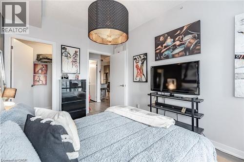 Bedroom featuring a striking black drum pendant light fixture with a metallic interior, light gray wall paint, and wood-finish flooring visible through the doorway - 85 Duke Street W Unit# 507, Kitchener, ON - Indoor Photo Showing Bedroom