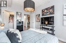 Bedroom featuring a striking black drum pendant light fixture with a metallic interior, light gray wall paint, and wood-finish flooring visible through the doorway - 