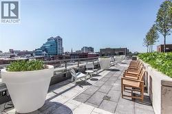 Expansive rooftop terrace featuring large format paver flooring, a glass railing system, and integrated planters with greenery - 