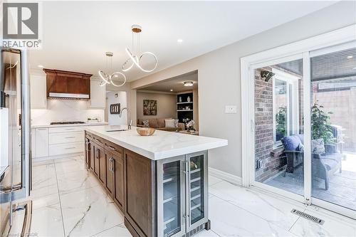 Spacious kitchen featuring an extended island with a built-in beverage cooler, white cabinetry, a wood-finish range hood, stainless steel appliances, and large format white tile flooring - 1264 Kane Road, Mississauga, ON - Indoor Photo Showing Kitchen