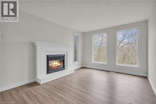 Spacious interior featuring a white mantel fireplace with a black firebox, multiple large windows, wood-finish flooring, and white baseboards - 22 Blackhorne Crescent, Kitchener, ON - Indoor Photo Showing Living Room With Fireplace