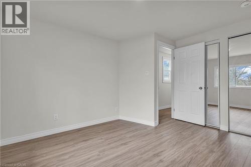 Neutral-toned interior featuring wood-finish flooring, white baseboards, and a white paneled door - 22 Blackhorne Crescent, Kitchener, ON - Indoor Photo Showing Other Room