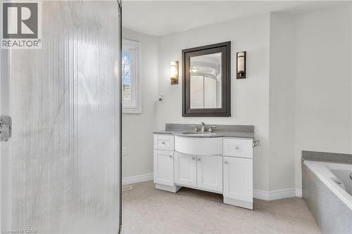 Bathroom vanity with a curved sink, stone countertop, white cabinetry, and wall-mounted sconces - 22 Blackhorne Crescent, Kitchener, ON - Indoor Photo Showing Bathroom