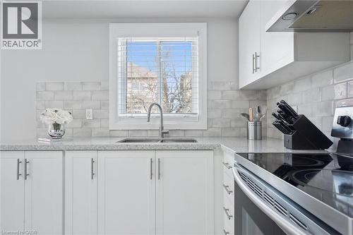 Modern kitchen featuring white cabinetry, light-toned countertops, a stainless steel sink with a gooseneck faucet, a subway tile backsplash, and a built-in stainless steel range - 5449 Rochelle Way, Mississauga, ON - Indoor Photo Showing Kitchen With Double Sink