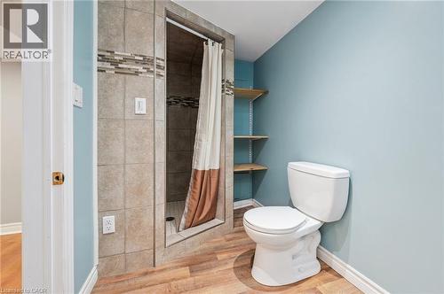 Three-piece bathroom featuring a tiled shower stall with a decorative accent band, a white toilet, and wood-finish flooring - 838 Moore Street, Cambridge, ON - Indoor Photo Showing Bathroom