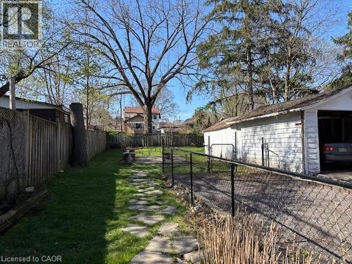 Expansive backyard featuring a stone pathway, mature trees, manicured lawn, and a detached two-car garage with a chain-link fence - 838 Moore Street, Cambridge, ON - Outdoor