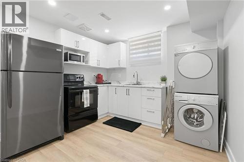 Kitchen with stainless steel appliances, white cabinetry, stacked washer / dryer, light wood-style floors, and modern cabinets - 17 Clearview Drive, Hamilton, ON - Indoor Photo Showing Laundry Room