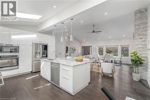 Open-concept living area with vaulted ceilings, dark wood-finish flooring, and a kitchen featuring a large central island with a sink, white cabinetry, and stainless steel appliances - 2123 Deyncourt Drive, Burlington, ON - Indoor Photo Showing Kitchen With Upgraded Kitchen