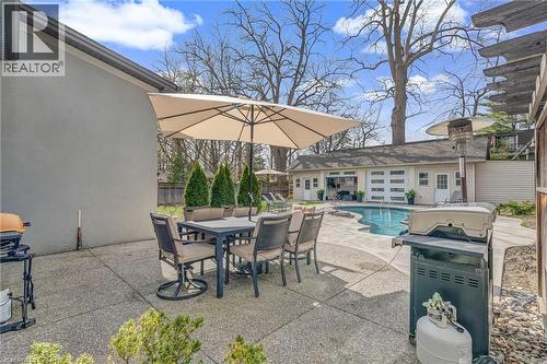Poolside patio featuring a freeform pool, surrounding concrete patio, and a detached structure with multiple garage doors - 2123 Deyncourt Drive, Burlington, ON - Outdoor With In Ground Pool