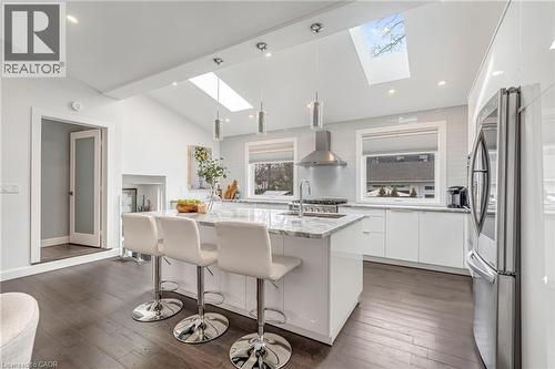 Open-concept kitchen featuring an oversized island with seating, a vaulted ceiling with skylights, stainless steel appliances, and wood-finish flooring - 2123 Deyncourt Drive, Burlington, ON - Indoor