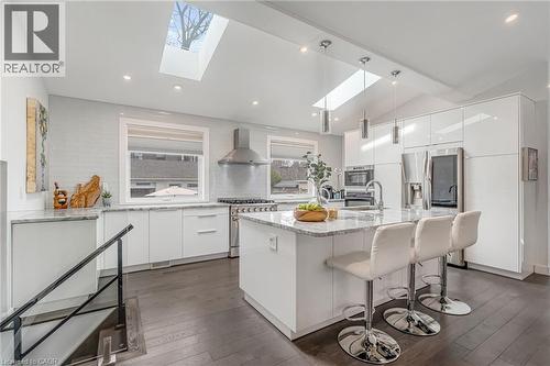 Bright kitchen featuring wood-finish flooring, white cabinetry, integrated stainless steel appliances, a center island with countertop seating, and multiple skylights - 2123 Deyncourt Drive, Burlington, ON - Indoor Photo Showing Kitchen With Upgraded Kitchen