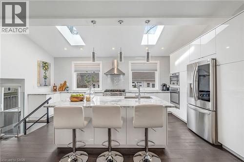 Contemporary kitchen featuring a large central island with seating, white high-gloss cabinetry, stainless steel appliances, and skylights - 2123 Deyncourt Drive, Burlington, ON - Indoor