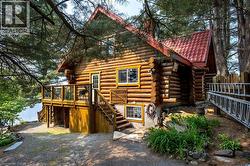 Log cabin exterior featuring a red tile roof, raised wood deck with glass panel railings, and a wooden staircase - 